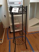 Side view of charcoal metal plant stand on wooden floor showing scrollwork and circular base