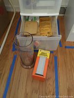 Photo of plastic graduated measuring cylinders, one cylindrical glass container, and photographic paper packets in a drawer