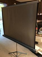 Front view of Da Lite Silver Light gray projection screen mounted on tripod stand in a room.