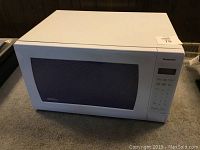 Front angled view of the white Panasonic microwave on carpeted floor with visible control panel and door.
