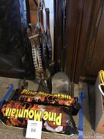 Photo of two Pine Mountain artificial logs next to fireplace tools including bellows, shovel, brush, poker, and log tongs on metal stand with goose-themed damper hook.