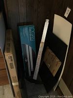 Photo shows boxed Logan Mat Cutter, other unboxed rulers, T-squares and foam boards stored vertically against a paneled wall.