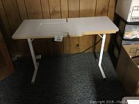 Full view of white folding sewing table with composite board top showing raised platform for sewing machine with cutout section.