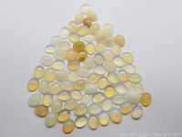 Top view of approximately 97 oval cabochon Ethiopian opals arranged in a loose pile exhibiting yellow, milky white translucent colors and light flash.