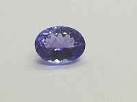 Close-up front view of an oval blue tanzanite gemstone against a white background showing color and faceting.