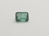 Front and slightly angled view of a loose emerald cut deep green emerald showing size, shape, and internal characteristics