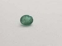 Close-up front view of oval green Colombian emerald gemstone on white background highlighting the green transparency and natural inclusions.
