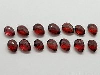Top view of fourteen faceted deep red garnet gemstones arranged in a line, showing their rich color and shape.