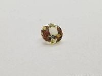 Close-up of the light yellow Ceylon sapphire showing the diamond cut facets with a round shape on plain white background.