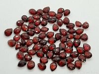 Pile of dark red pear-shaped checker cut garnet gemstones laid out on white background, showing facets and color depth.