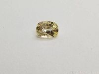 Front angle image of light yellow cushion cut sapphire on white background showing clarity and color
