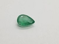 Top view of pear cut Colombian emerald on white background showing shape and clarity.