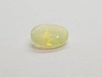 Oval cut translucent Ethiopian opal gemstone showing yellow rolling flash play of color on plain white background.
