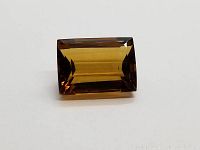 Emerald-cut deep golden citrine gemstone displayed on white background showing the facets and color.