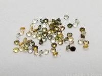 Loose mixed color diamond cut tourmaline gemstones scattered on a white background, showing a variety of colors and faceted cuts.