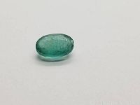 Oval cut blue-green Colombian emerald on white background, showing color and clarity.