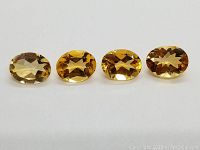 Four oval calibrated Brazilian Citrines displayed on white background showing front and top faceted surfaces with golden yellow color.