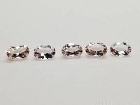 Five oval faceted morganite gemstones arranged in line on a white background showing their light mixed colors and size.