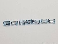 Top-down view of seven emerald cut blue topazes arranged in a straight line on white background