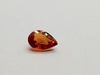 Photo showing a pear cut orange sapphire gemstone with good clarity and reflective facets on a white background.