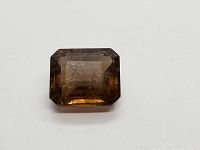 Front view of the large emerald cut cognac tourmaline showing clarity and color under direct light on white background.