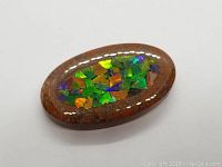 Close-up of the oval cabochon stone with green, orange, and purple mosaic ammolite inlay on a brown base.