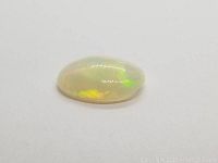 Close-up side view of the oval cabochon crystal opal showing its translucent body and bright play of colors.