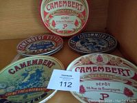 Image showing four dessert cheese plates, each with distinct vintage French cheese labels, and a round storage box also with Camembert label.