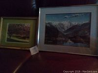 Photo showing two framed pieces of art: on the left, a smaller framed photo of a tree with pink blossoms representing Early Spring Evening in High Park; on the right, a larger framed print of a mountain landscape reflecting on water titled The Lions Peaks.