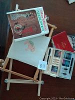 Needlepoint book, two needlepoint frames, needlepoint fabric, calligraphy kit with instruction booklet and supplies on table