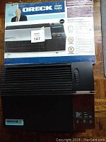 Photo showing one Oreck XL professional air purifier in black with original box behind it.