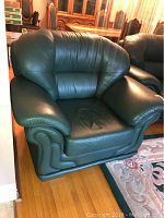 Green leather armchair angled view showing cushioned backrest, armrest, and front base details