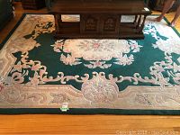 Full view of rectangular floral area rug under wooden coffee table, showing overall design and colors.