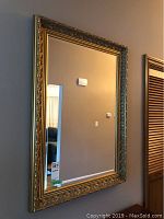 Front view of framed bevelled wall mirror showing detailed ornate gold-tone embossed frame and bevelled glass.