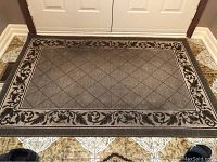 Larger gray area rug with diamond lattice center and floral border placed on tiled floor in front of double doors