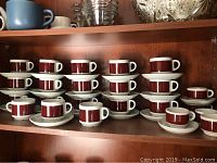 Shelf with multiple maroon and white espresso and cappuccino cups stacked on white saucers.
