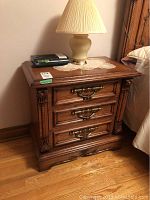 Front view of one wooden night table with three drawers showing brass handles and decorative carved accents
