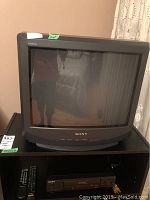 Front view of Sony Trinitron 20 inch TV on stand with Sony VCR below, showing screen and front control buttons with remotes.