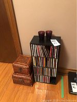 Front view of CD rack containing CDs, two keepsake boxes to the left, and two purple glass candles on top of the rack.