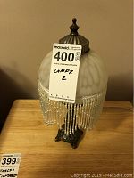 Vintage table lamp with frosted glass dome shade and beaded fringe on a dark ornate metal base. Untested condition, some wear visible.
