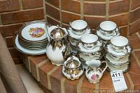 Full view of the Bavaria china tea set stacked and arranged with silver serving pieces on brick hearth.