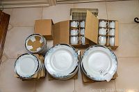 Full view of plates stacked along with boxed cups on tile floor.