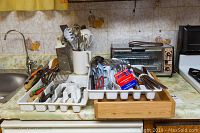 Photo of kitchen counter with utensil organizer trays filled with flatware, serving spoons, scissors, cheese shredder, and General Electric toaster visible.