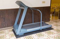 Full side view of gray PaceMaster treadmill with metal handrails, placed on a black mat on patterned flooring.