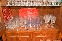 Glassware on wooden shelf showing crystal stem wine glasses, textured tumblers, and Christmas trays at back
