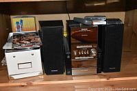 Full view of the Panasonic stereo system with speakers, remote, and CDs displayed on a wooden shelf.