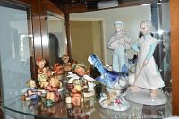View of all porcelain figurines displayed on glass shelf including the Goebel Hummel figurines and other signed porcelain pieces
