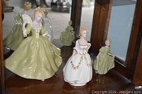 Three hand painted china figurines depicting women in period dresses positioned together in a display cabinet.