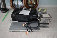 Black HP Photosmart C4640 printer with manuals on top, silver JVC DVD player in front, RCA cables placed on DVD player, and multiple stacks of CDs to side.