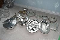 Overview of multiple silver plated serving trays, chafing dishes, sugar and creamer, and a vintage aluminum lidded serving bowl, showing all items and their arrangement.